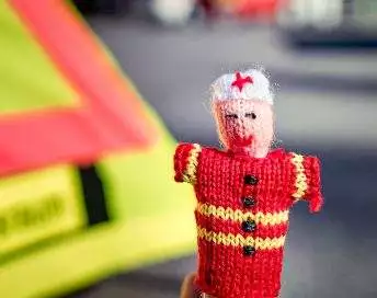 Strickpüppchen eines Notfallsanitäters mit roter Uniform und unscharfem Hintergrund.