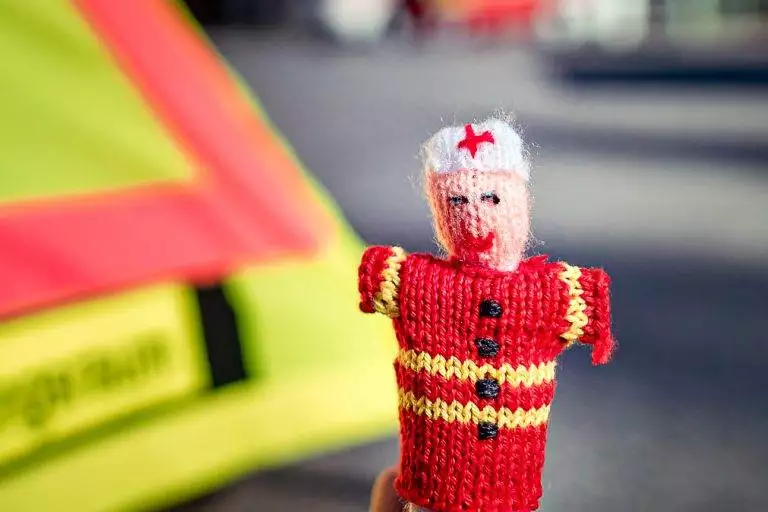 Strickpüppchen eines Notfallsanitäters mit roter Uniform und unscharfem Hintergrund.
