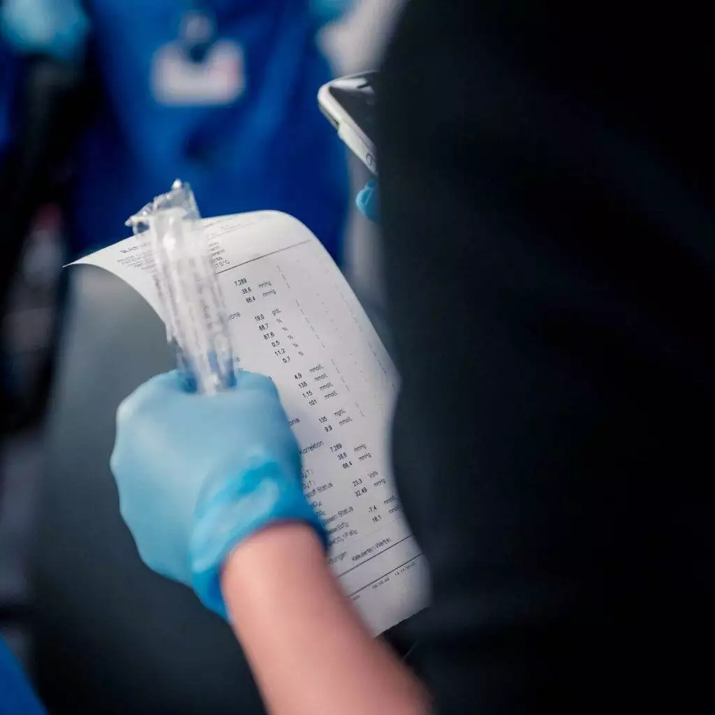 Das Bild zeigt eine Krankenschwester, die eine Spritze und ein Papier mit dem Blutwerten hält.