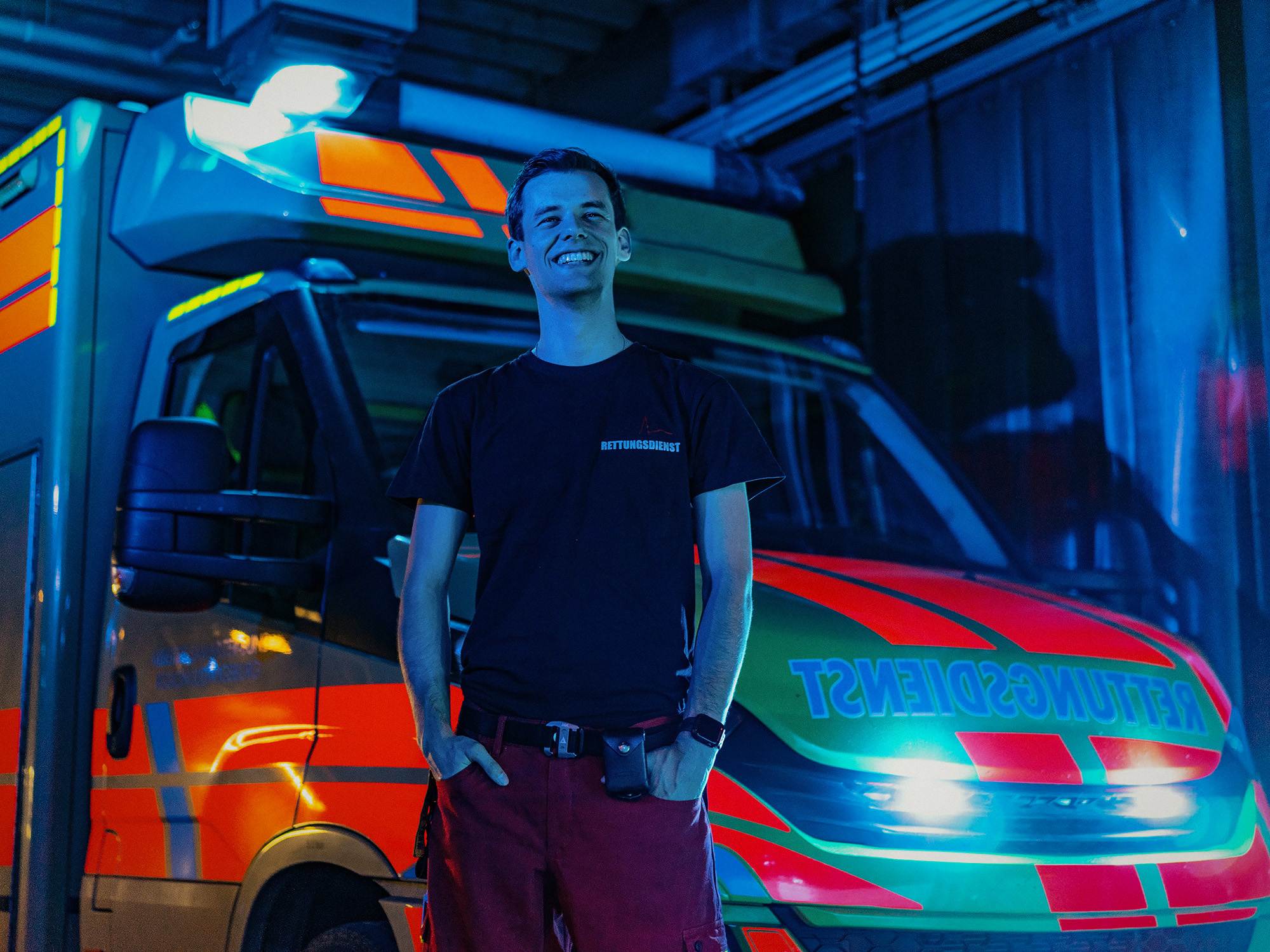 Bild des Leihkraftes von Hire a Paramedic. Er steht vor dem Krankenwagen in seiner Uniform und lächelt.