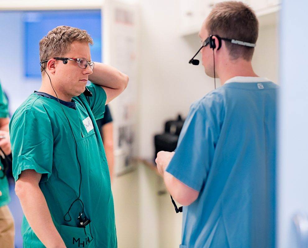 Anästhesistische Assistent und Führungskraft besprechen Angelegenheiten miteinander. Der eine trägt einen grünen Kittel, die andere einen blauen Kittel.