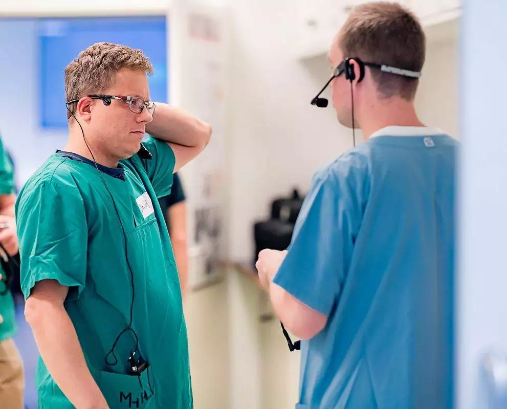 Anästhesistische Assistent und Führungskraft besprechen Angelegenheiten miteinander. Der eine trägt einen grünen Kittel, die andere einen blauen Kittel.
