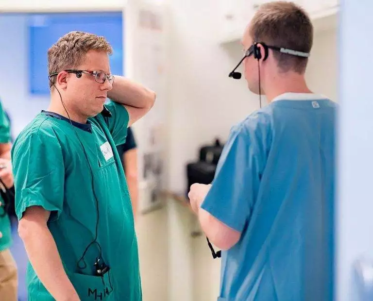 Zwei Physician Assitant besprechen Angelegenheiten miteinander. Der eine trägt einen grünen Kittel, die andere einen blauen Kittel.