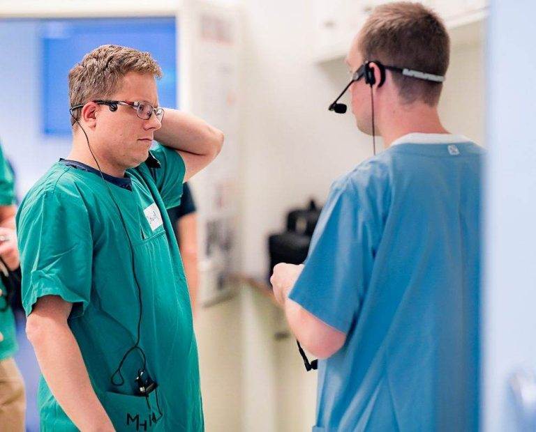 Zwei Ärzte in der Klinik besprechen Angelegenheiten miteinander. Eine trägt einen grünen Kittel, die andere einen blauen Kittel.