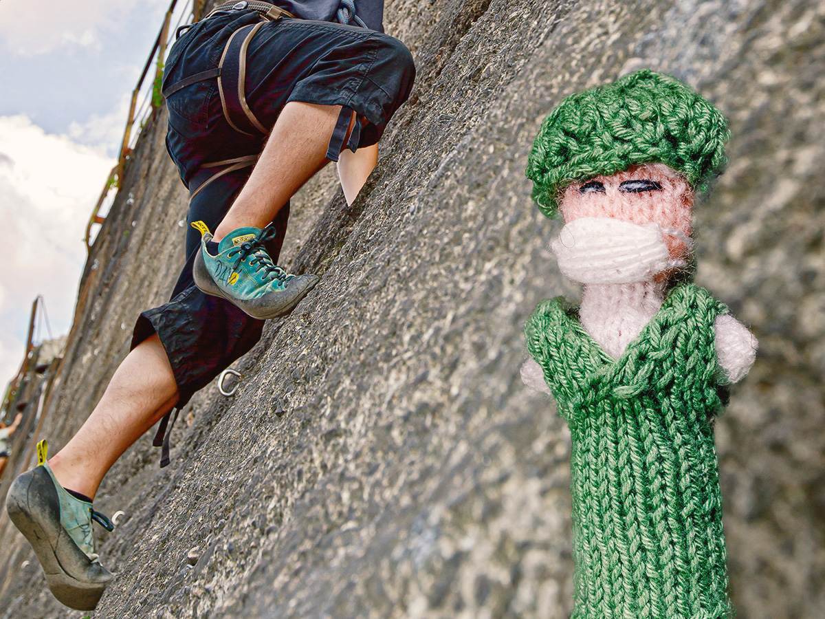 Strickpüppchen einer Pflegefachkraft, sie trägt einen grünen Kittel. Im Hintergrund ist ein Mann beim Klettern zu sehen, was das Bild der Work-Life-Balance in der Zeitarbeit symbolisiert