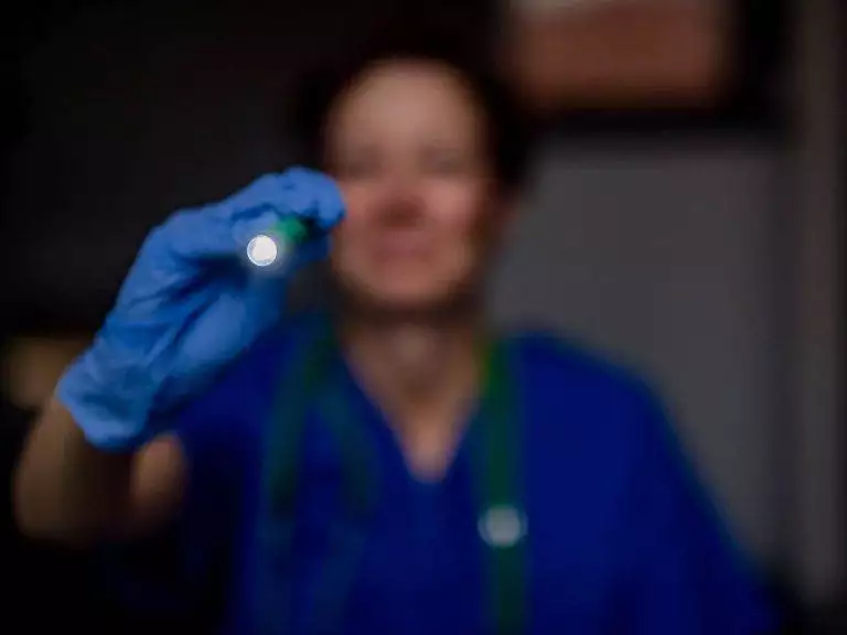 Pflegefachkraft mit Taschenlampe in der Hand. Sie trägt einen blauen Kittel und hat ein Stethoskop um den Hals
